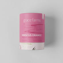 Load image into Gallery viewer, Grace Farms Hibiscus Orange Organic Herbal Tea in a pink cylindrical cardboard canister, shown on a neutral light gray background.
